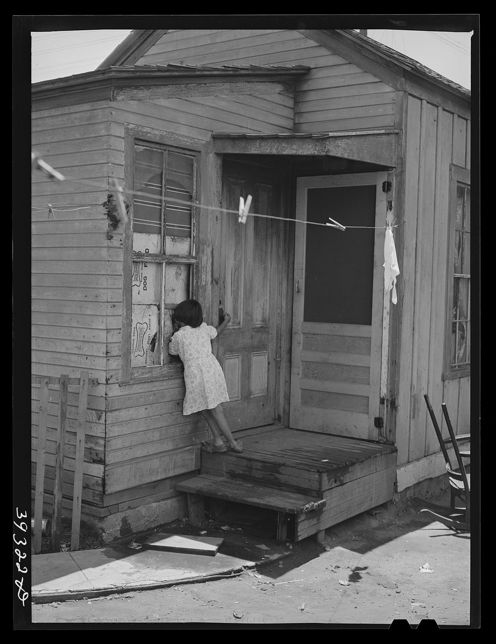 Little Mexican girl looking in window of her home. San Diego, California by Russell Lee