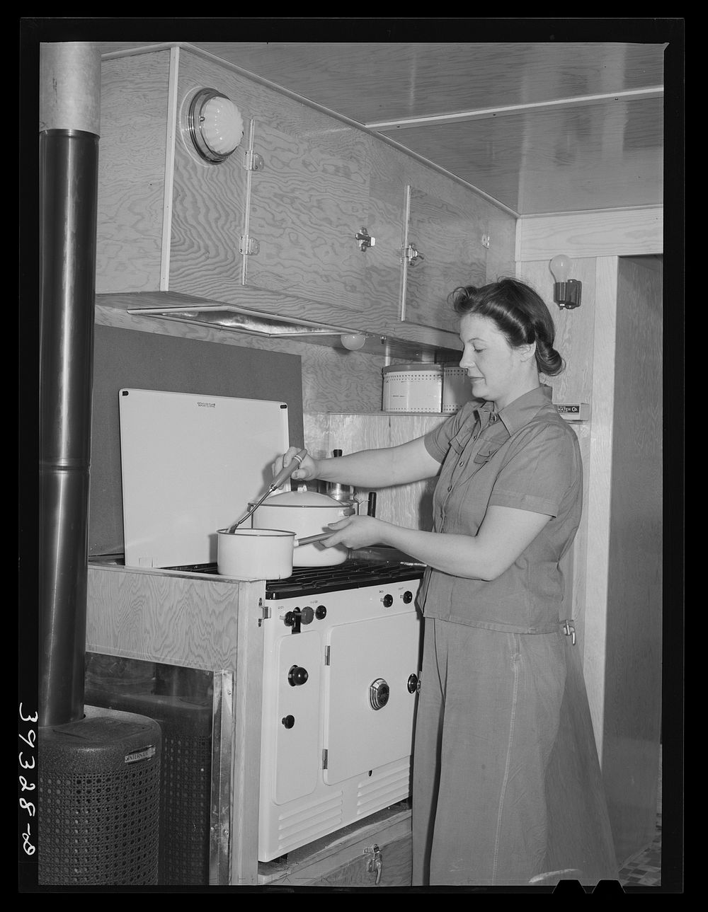 Wife of aircraft worker at the stove in her trailer home at the FSA (Farm Security Administration) camp for defense workers.…