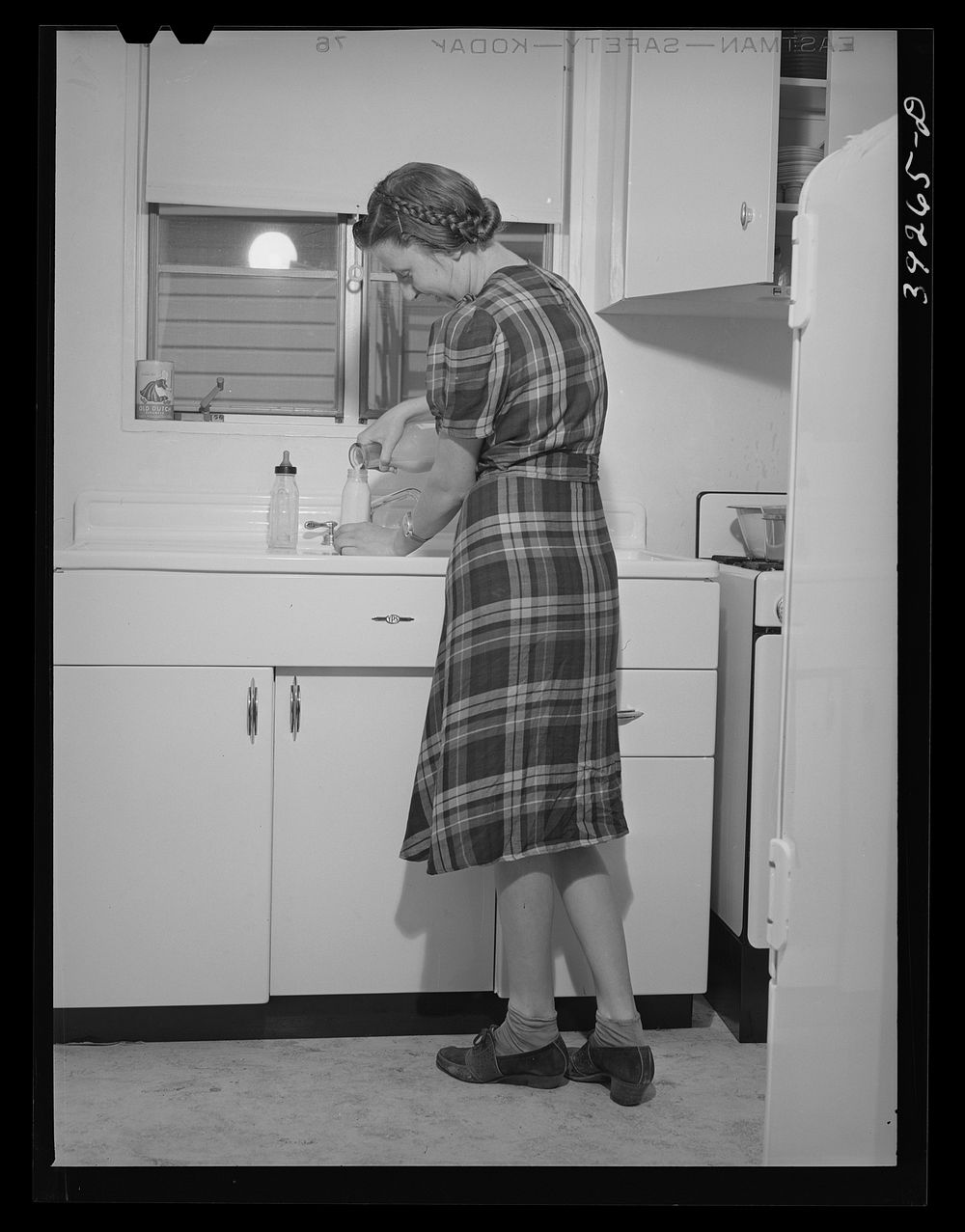 Mother preparing baby's bottle. She lives in one of the houses at the Kearney-Mesa defense housing project by Russell Lee