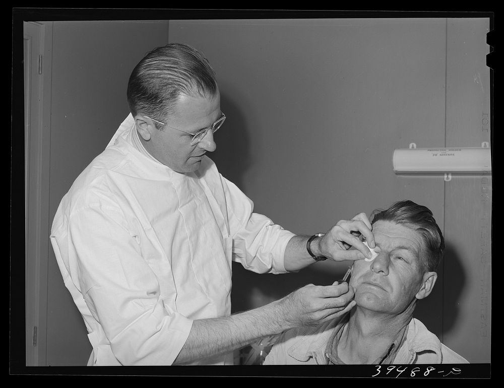 Doctor treats patient's eye (a minor burn) at the clinic at the FSA (Farm Security Administration) labor camp. Caldwell…