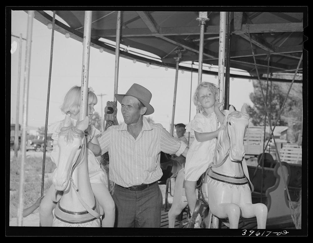 Father with his two daughters on the merry-go-round, one of the carnival attractions at the Fourth of July celebrations by…