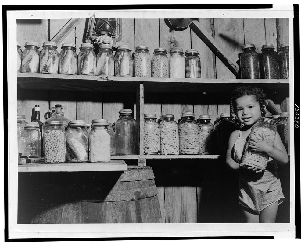 Dolores Harris, daughter of FSA (Farm Security Administration) client George Harris, with canned food prepared by her…