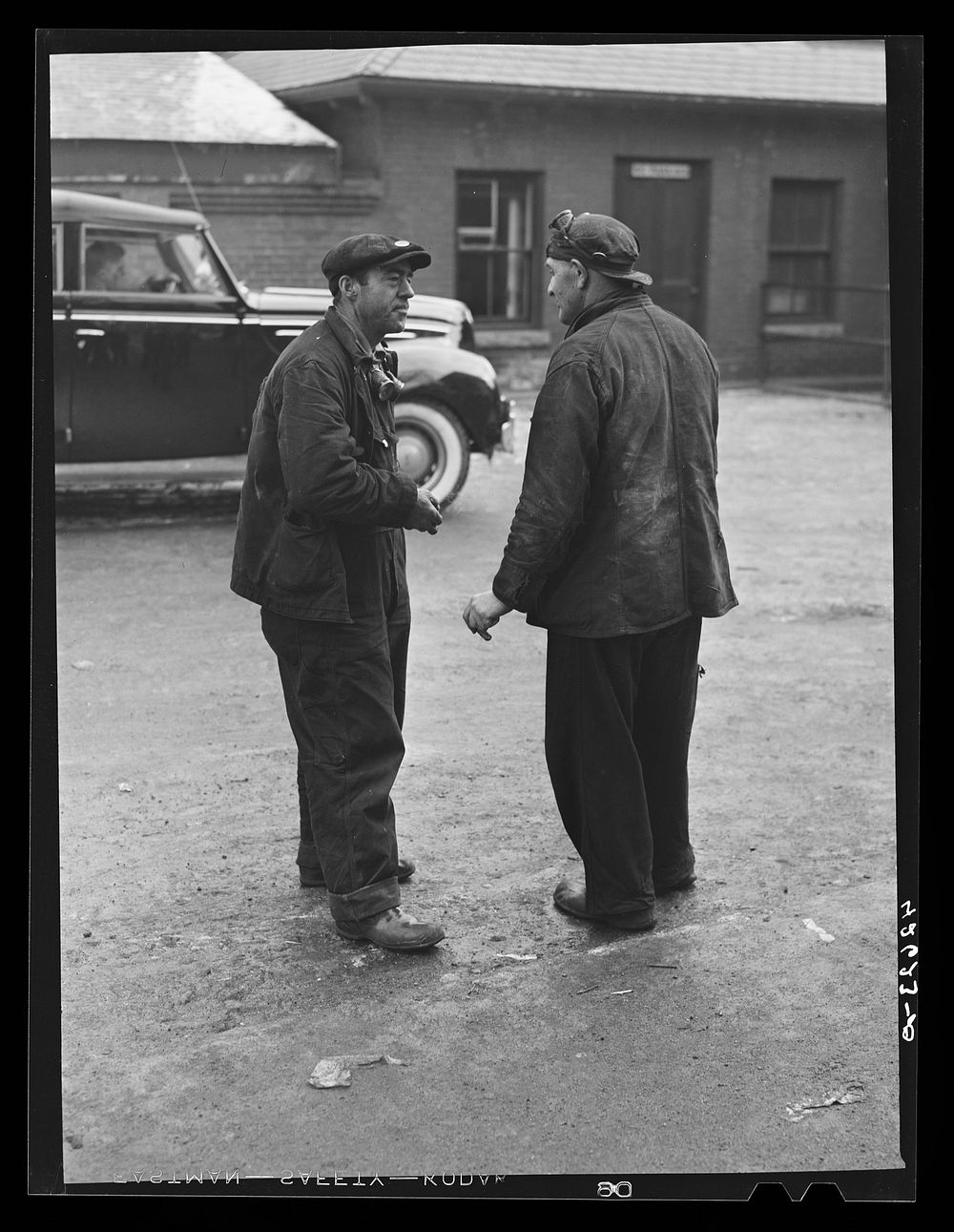 [Untitled photo, possibly related to: Two shipyard workers talking just outside the gates to the shipyard during lunch…
