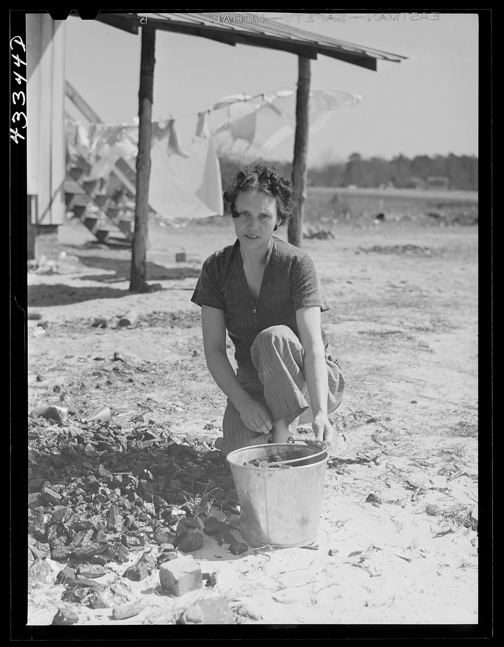 Woman who lives with her family in the upper part of tobacco barn, gathering coal. Husband works at Fort Bragg. Near…