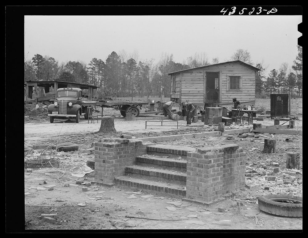 Moving a small outbuilding from the Santee-Cooper basin by means of a trailer truck. Near Bonneau, South Carolina. Sourced…