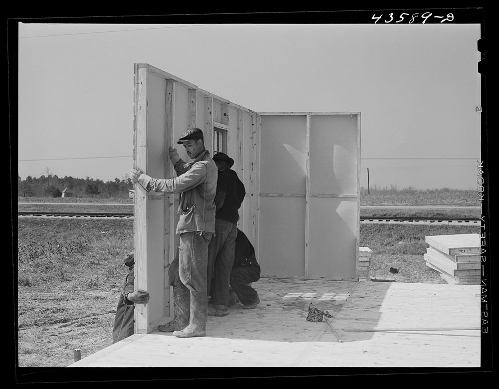 Putting up the first walls for FSA (Farm Security Administration) prefabricated houses for farmers who had to move out of…