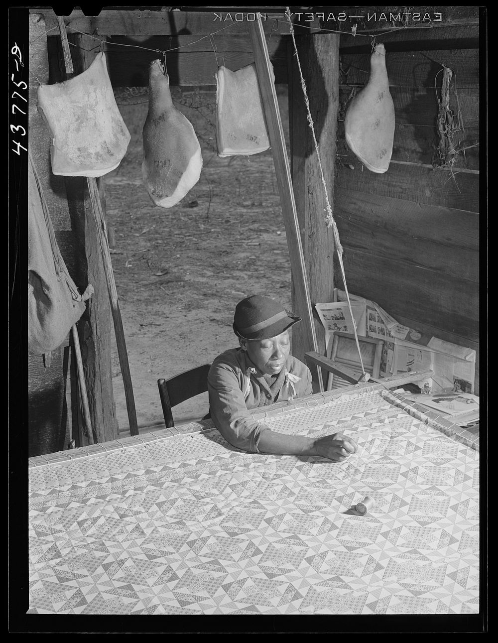 Woman who has not yet found a place to move out of the Hinesville Army camp area working on a quilt in her smokehouse. Near…