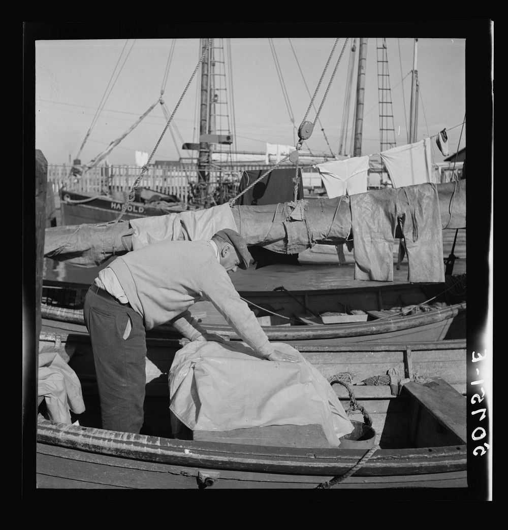 Fisherman oiling waterproof jackets and pants in boat. Christmas Day, Charleston, South Carolina. Sourced from the Library…