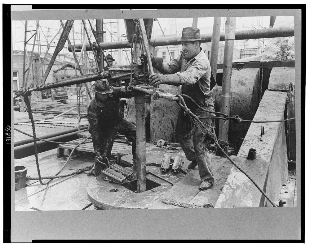Oil field workers adding a length of pipe to drill stream by means of heavy pipe wrenches, Kilgore, Texas by Russell Lee
