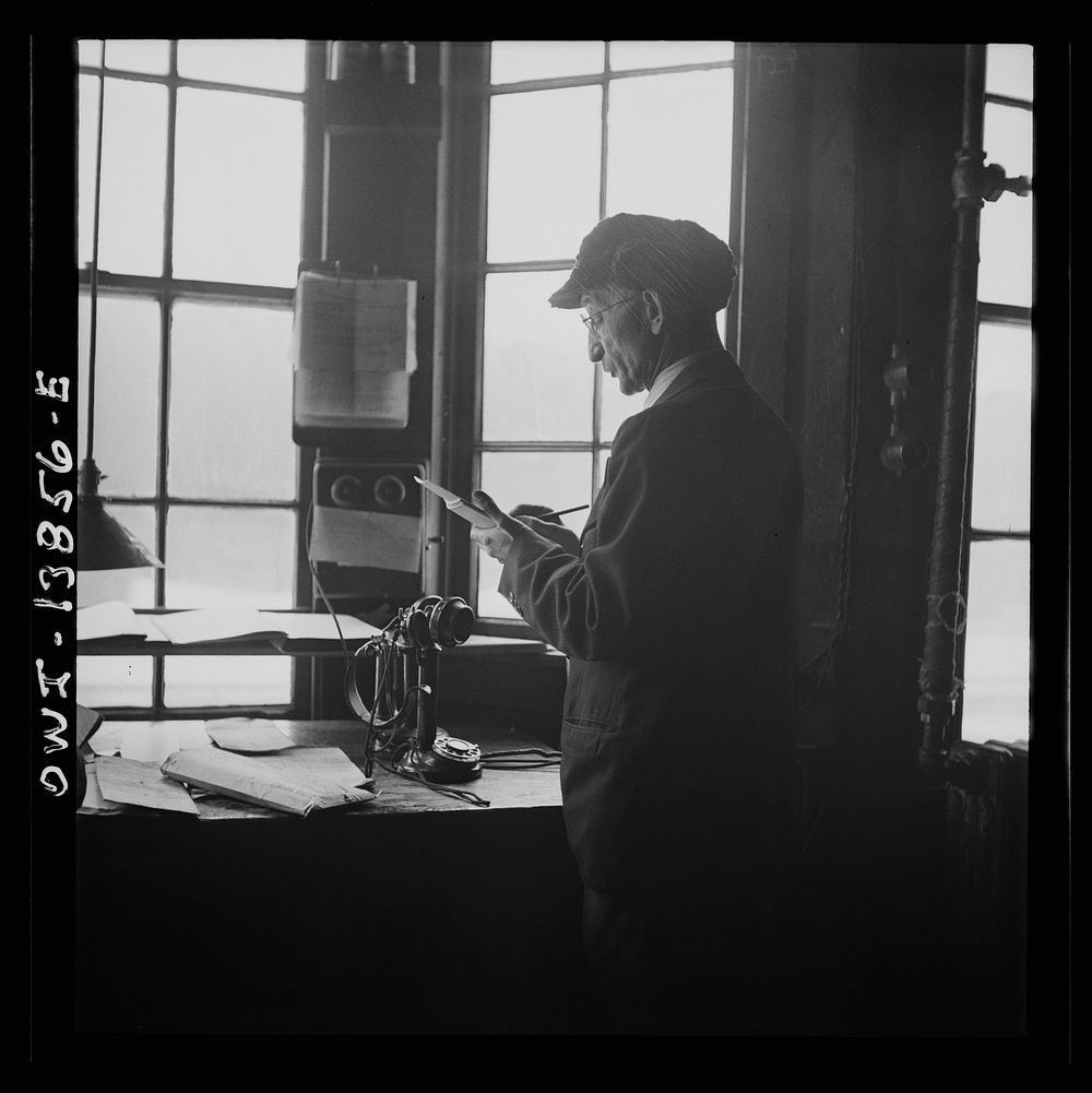 Chicago, Illinois. Yard clerk checking cars as trains are being made up outside his window. Sourced from the Library of…