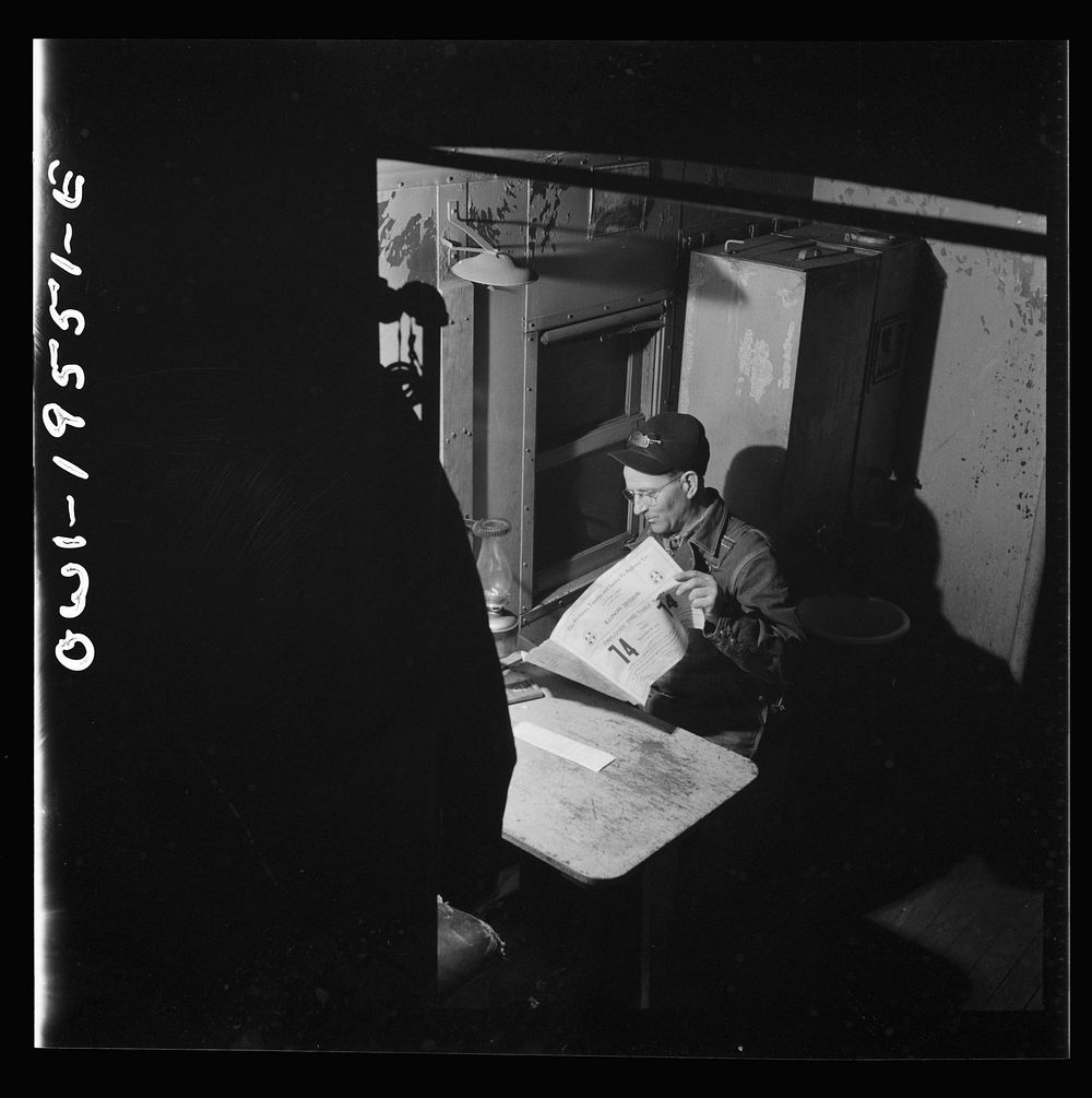 A conductor studying a timetable in the caboose on the Atchison, Topeka and Santa Fe Railroad between Chillicothe, Illinois…