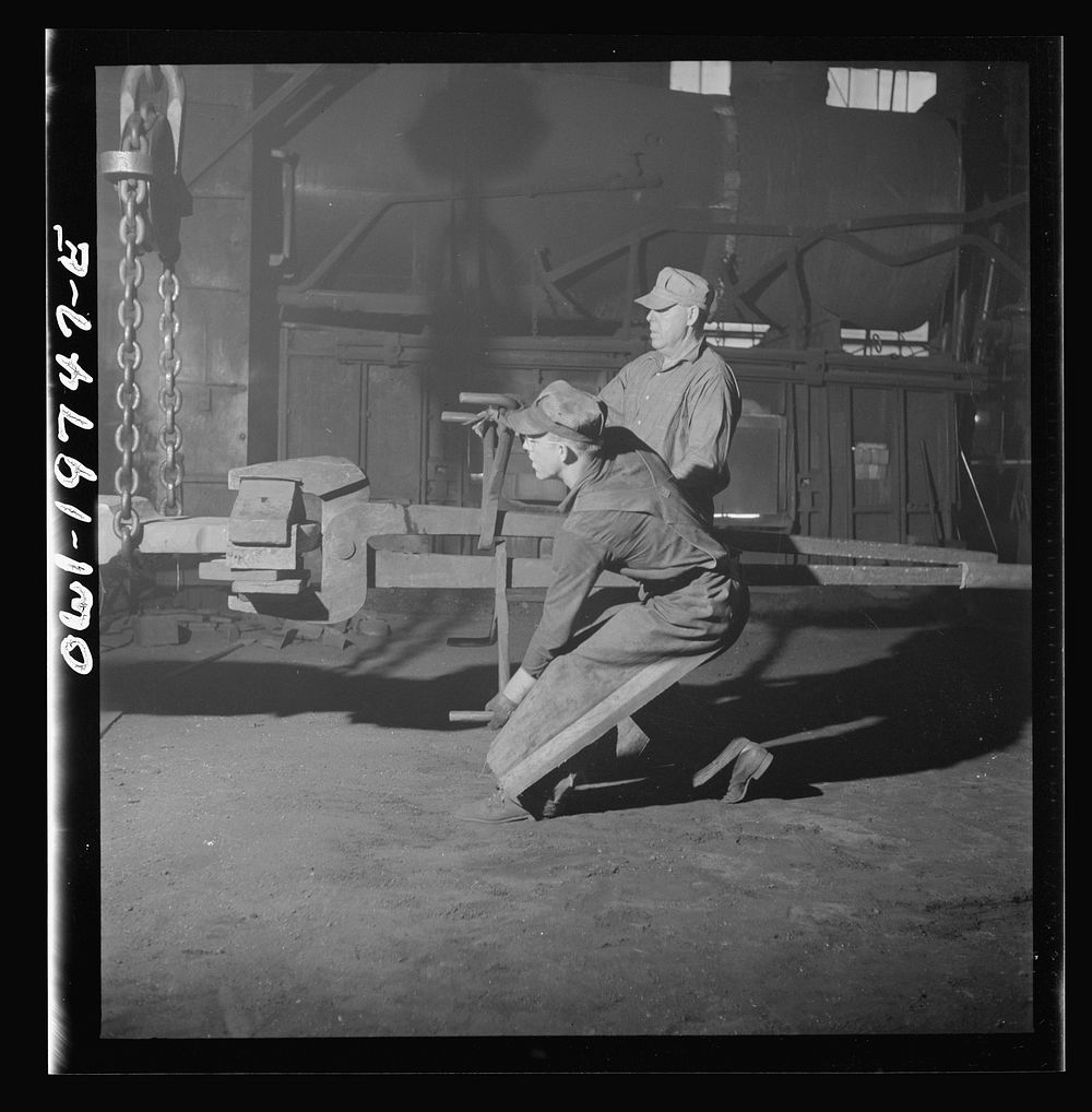 Topeka, Kansas. Workmen manipulating a hot forging which is being hammered under a steam hammer in the smith shop of the…