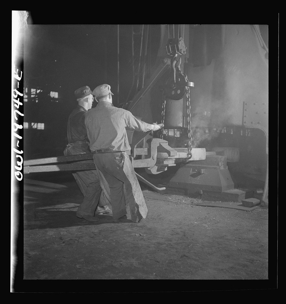 Topeka, Kansas. Workmen manipulating a hot forging which is being hammered under a steam hammer in the smith shop of the…