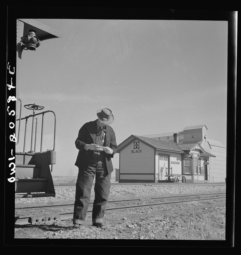 Black, Texas. Conductor reading his train orders as the train on the Atchison, Topeka, and Santa Fe Railroad between…