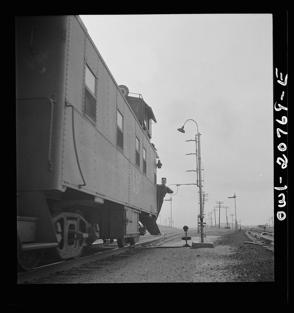 Isleta, New Mexico. Conductor of a passing freight train on the Atchison, Topeka and Santa Fe Railroad picking up a message.…