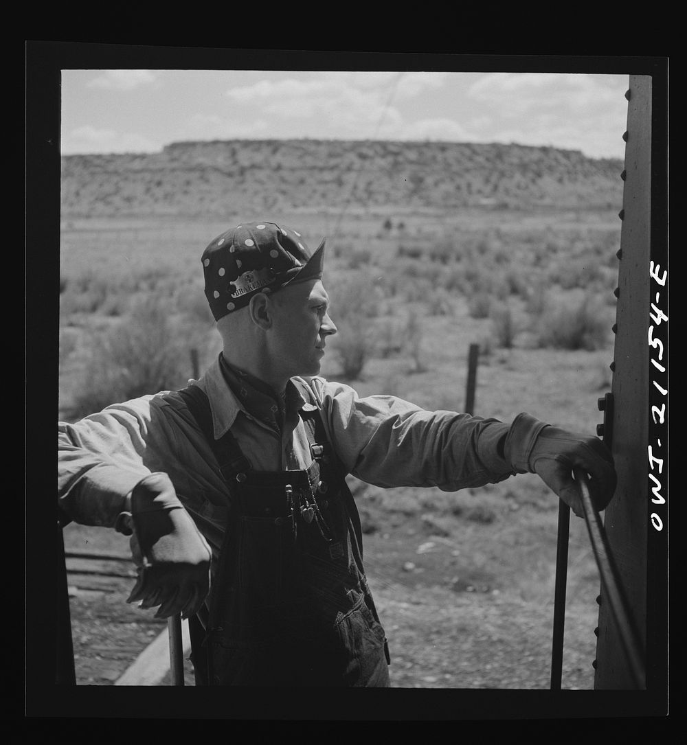 Acomita, New Mexico. Brakeman R.E. Capsey standing on the platform of the caboose waiting to hop off as the train on the…