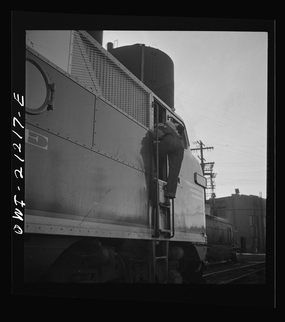 [Untitled photo, possibly related to: Winslow, Arizona. An engineer climbing into the cab of a diesel freight engine in the…