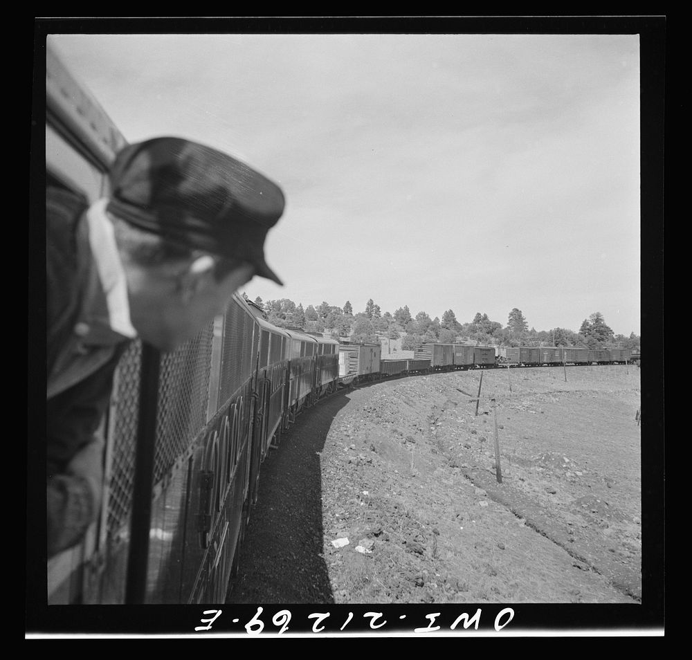 Williams, Arizona. A fireman watching a diesel freight train as it goes around a curve in the mountains on the Atchison…