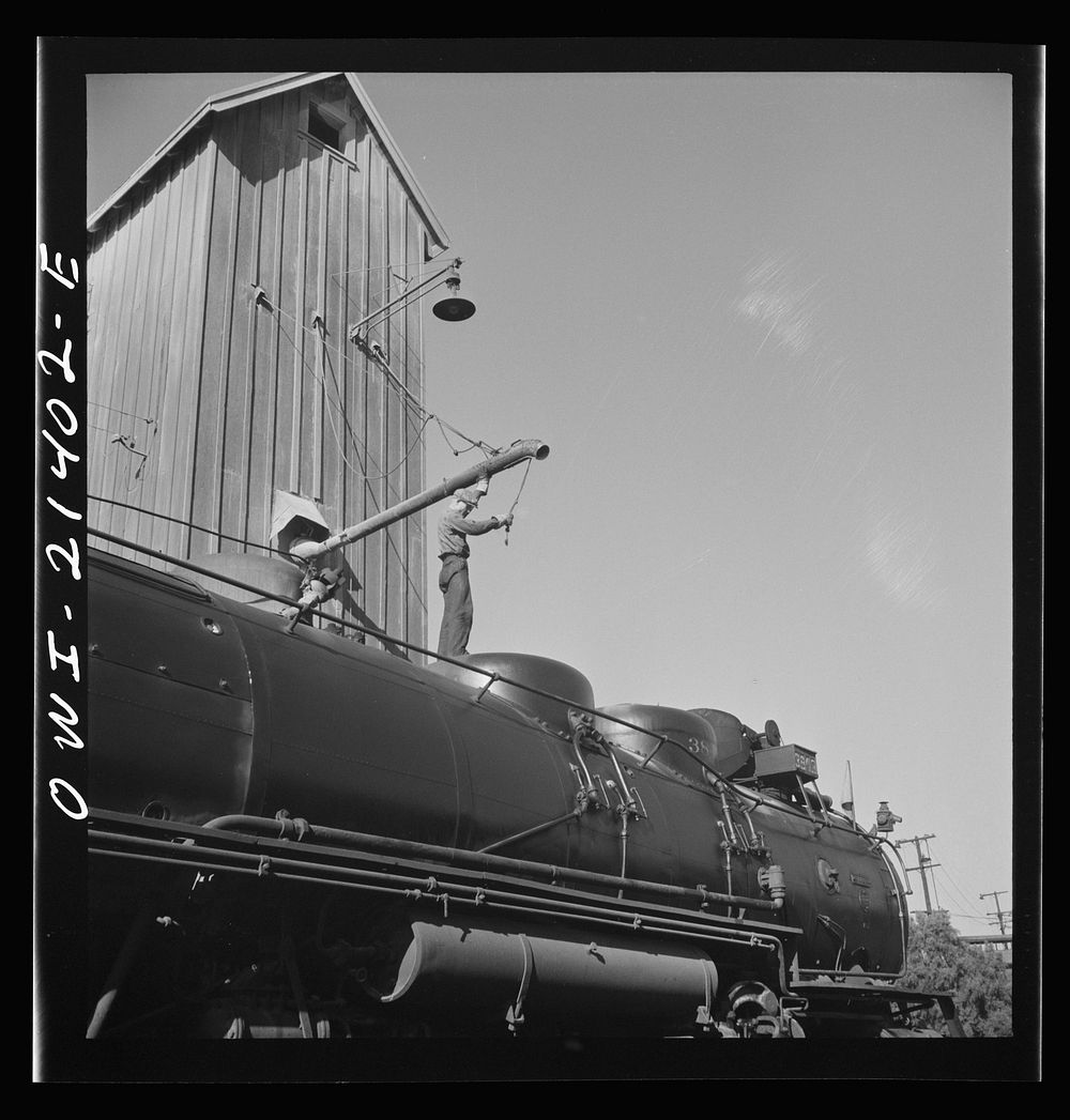 [Untitled photo, possibly related to: Needles, California. Filling the sand dome of a locomotive near the roundhouse in the…