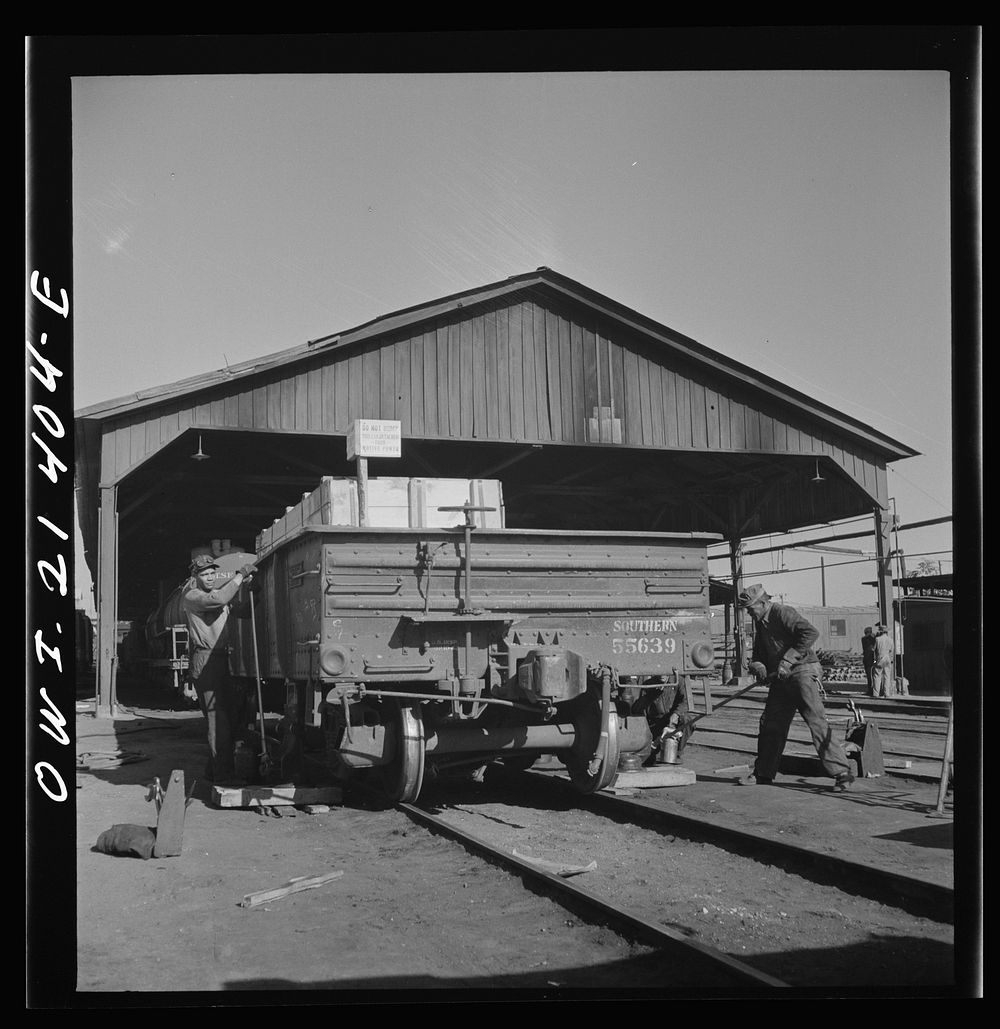 Needles, California. Workmen jacking up a car at the rip tracks in the Atchison, Topeka, and Santa Fe Railroad yard. Sourced…