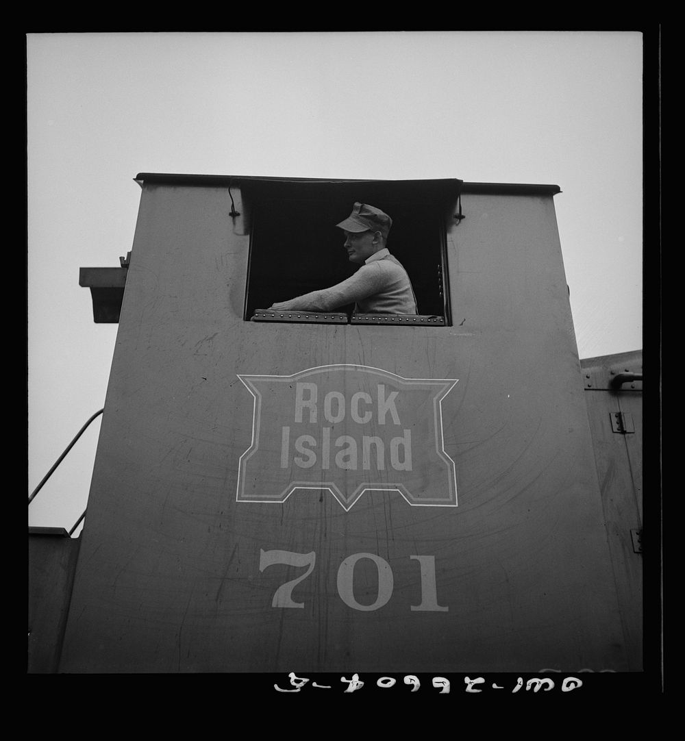 Blue Island, Illinois. Engineer in the cab of a diesel switch engine on the Chicago and Rock Island Railroad. Sourced from…
