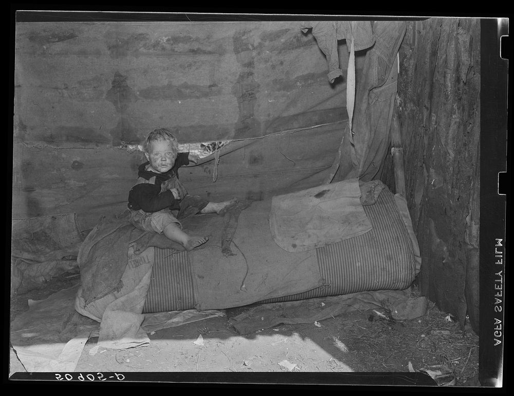 "Buddy," youngest child of migrant packinghouse worker from Tennessee, sitting on the only bed for six people, which is…