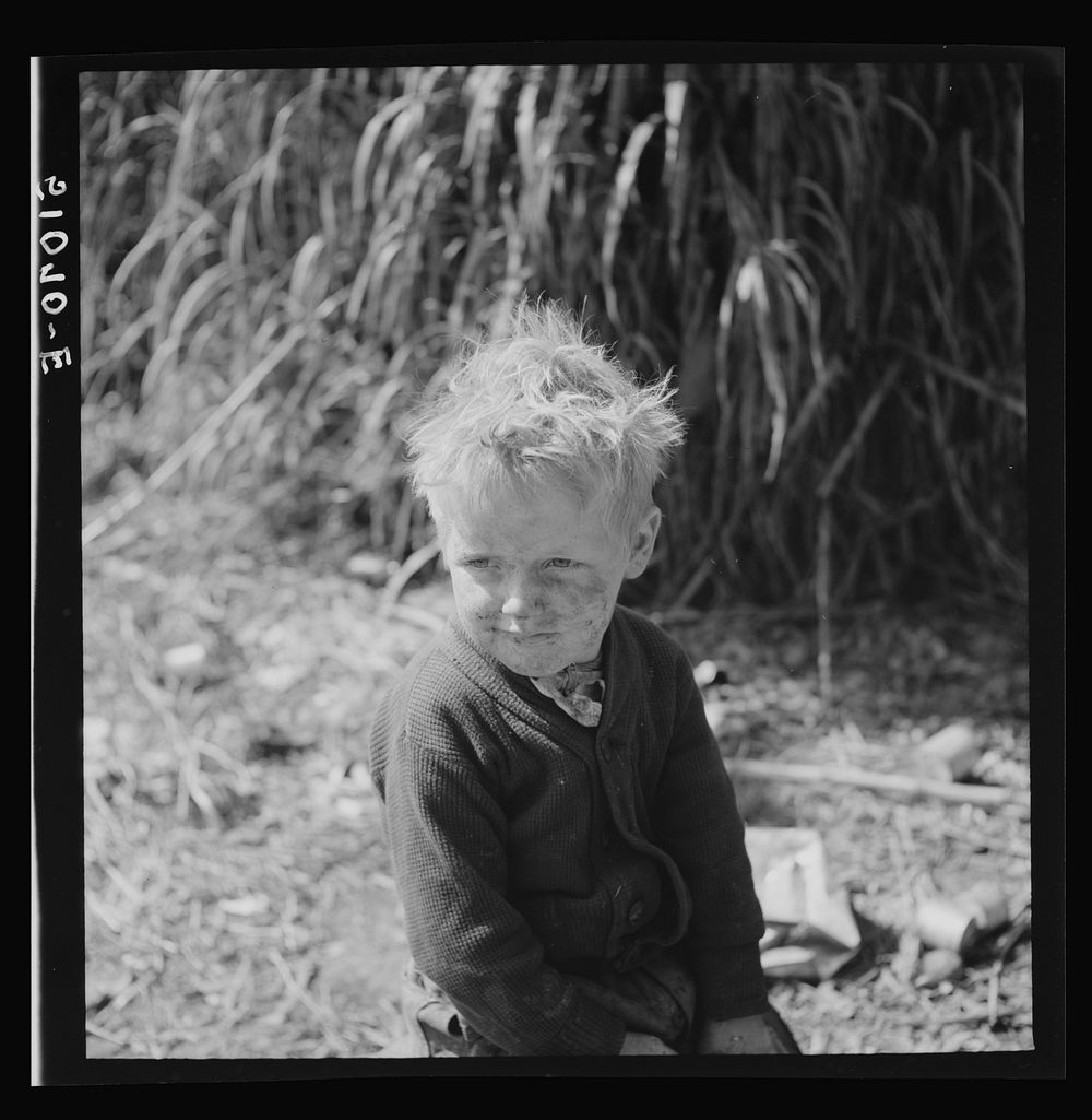 Child of packinghouse workers from Tennessee, his face covered with  muck which causes an itchy rash.  Belle Glade, Florida.…