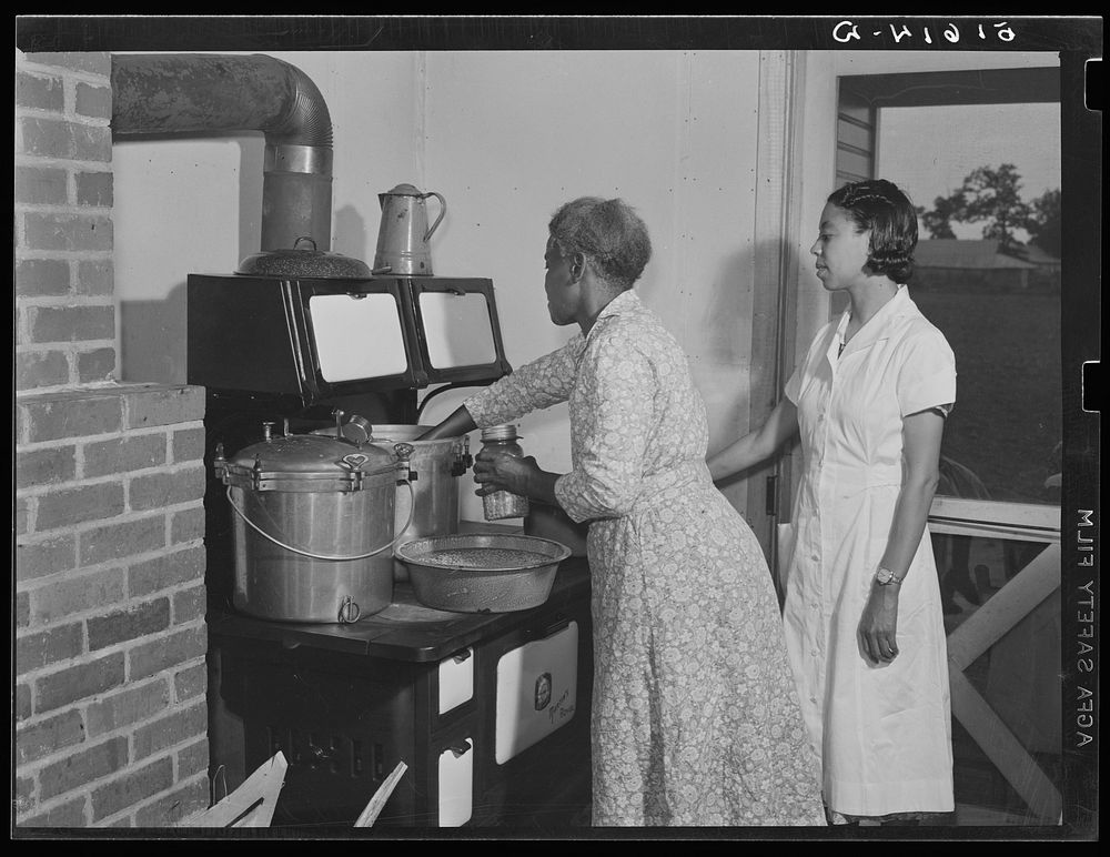 Ada Turner and Evelyn M. Driver home management and home economics supervisor, canning English peas with pressure cooker in…