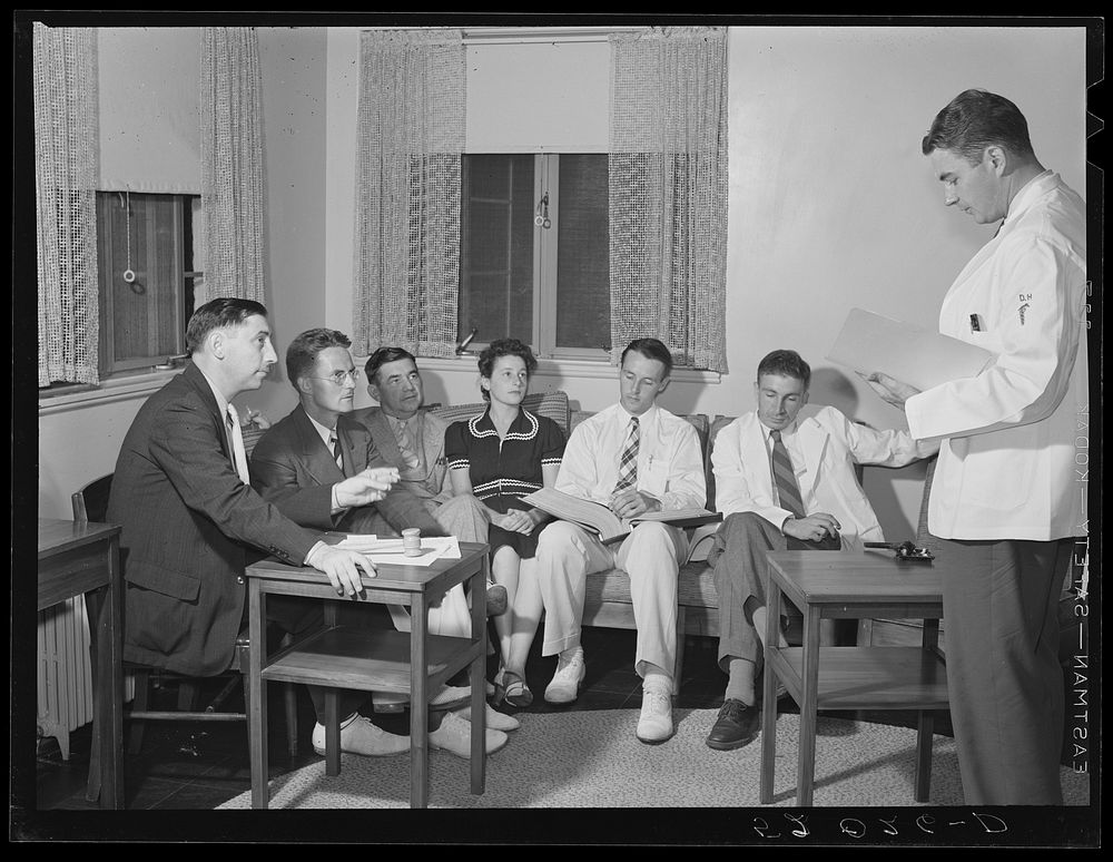 Doctor reading paper to members of board of directors of Greenbelt, Maryland medical association. Sourced from the Library…