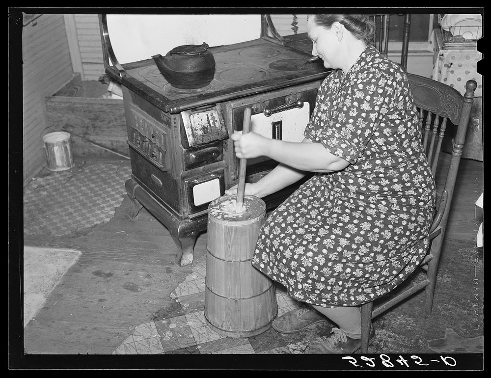 Mrs. Elvin Wilkins (Rosa) churning butter in the kitchen of their home in Tallyho, near Stem, Granville County, North…