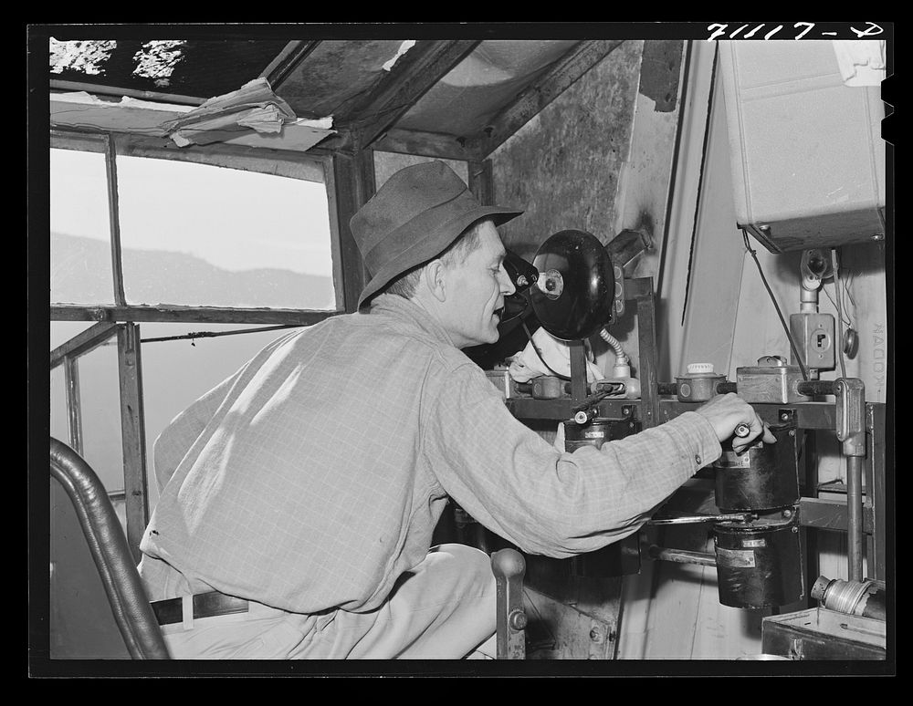 Man in control tower at Shasta Dam. Shasta County, California. He directs the various cable cars, equiptment which…