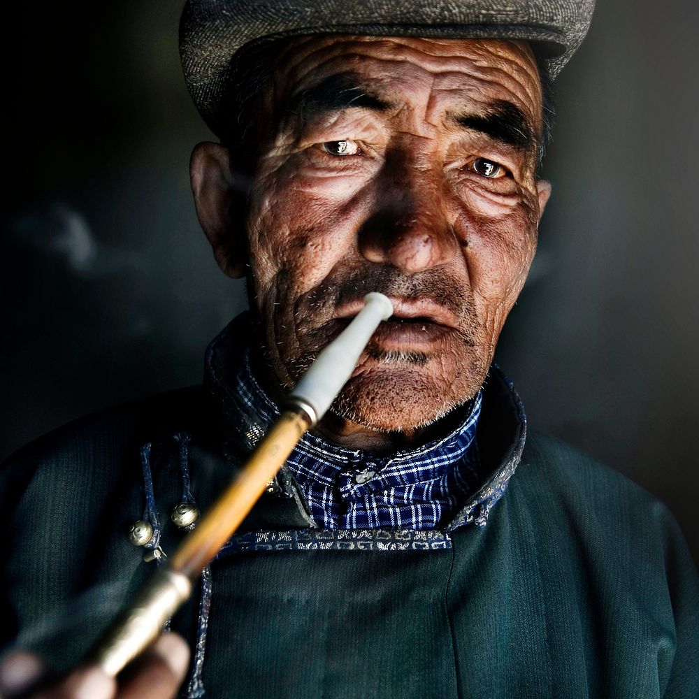 Mongolian man in traditional dress smoking a pipe.