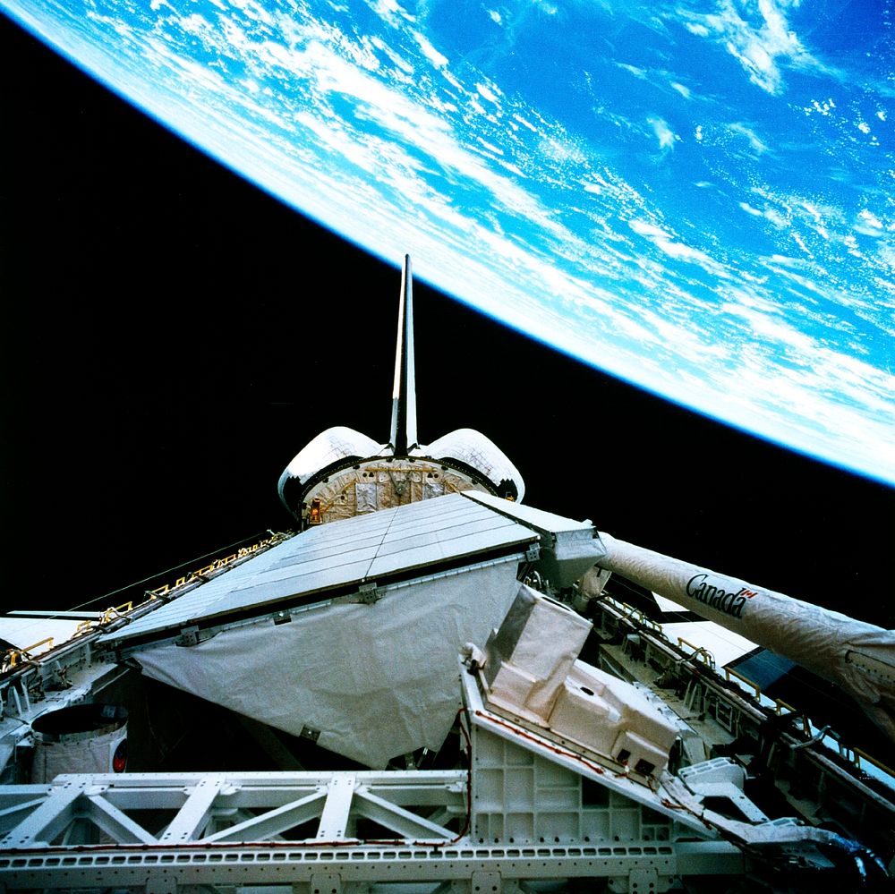 The payload bay of the orbiting space shuttle Endeavour with an area of the Pacific Ocean northeast of Hawaii in the…