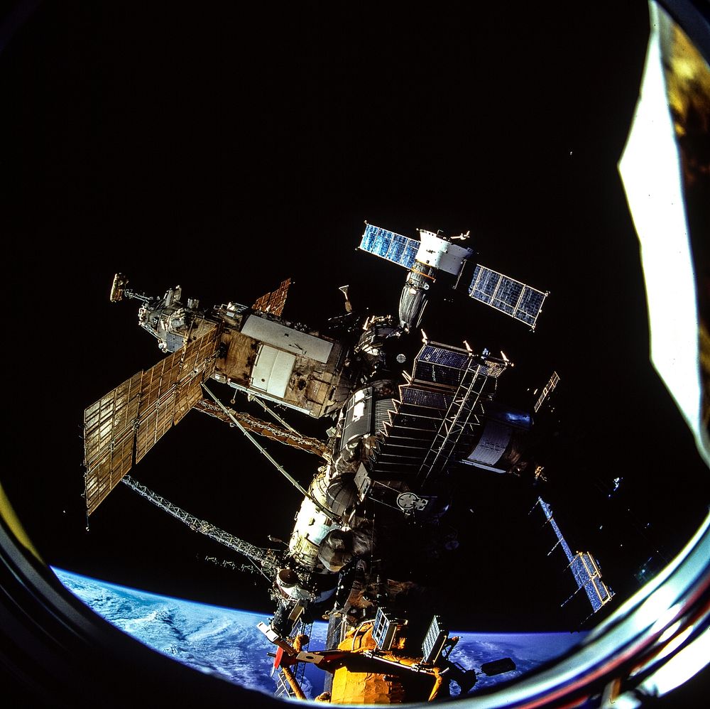 The docked Russian Mir Space Station is partially visible through the Spacehab viewing port. Original from NASA. Digitally…