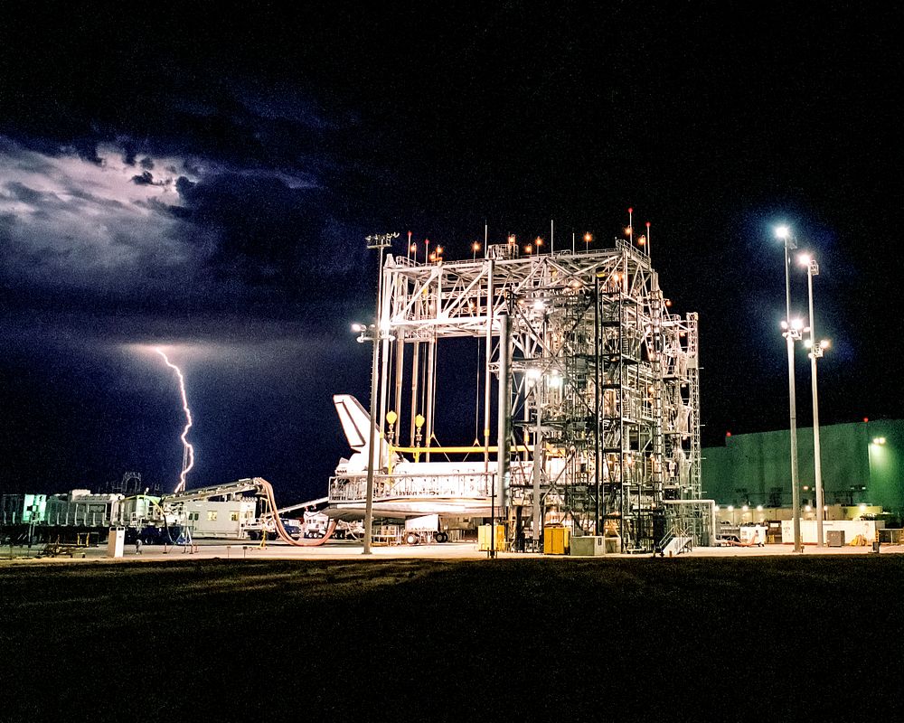 Lightning strikes in the distance as the Space Shuttle Discovery receives post-flight processing in the Mate-Demate Device.…