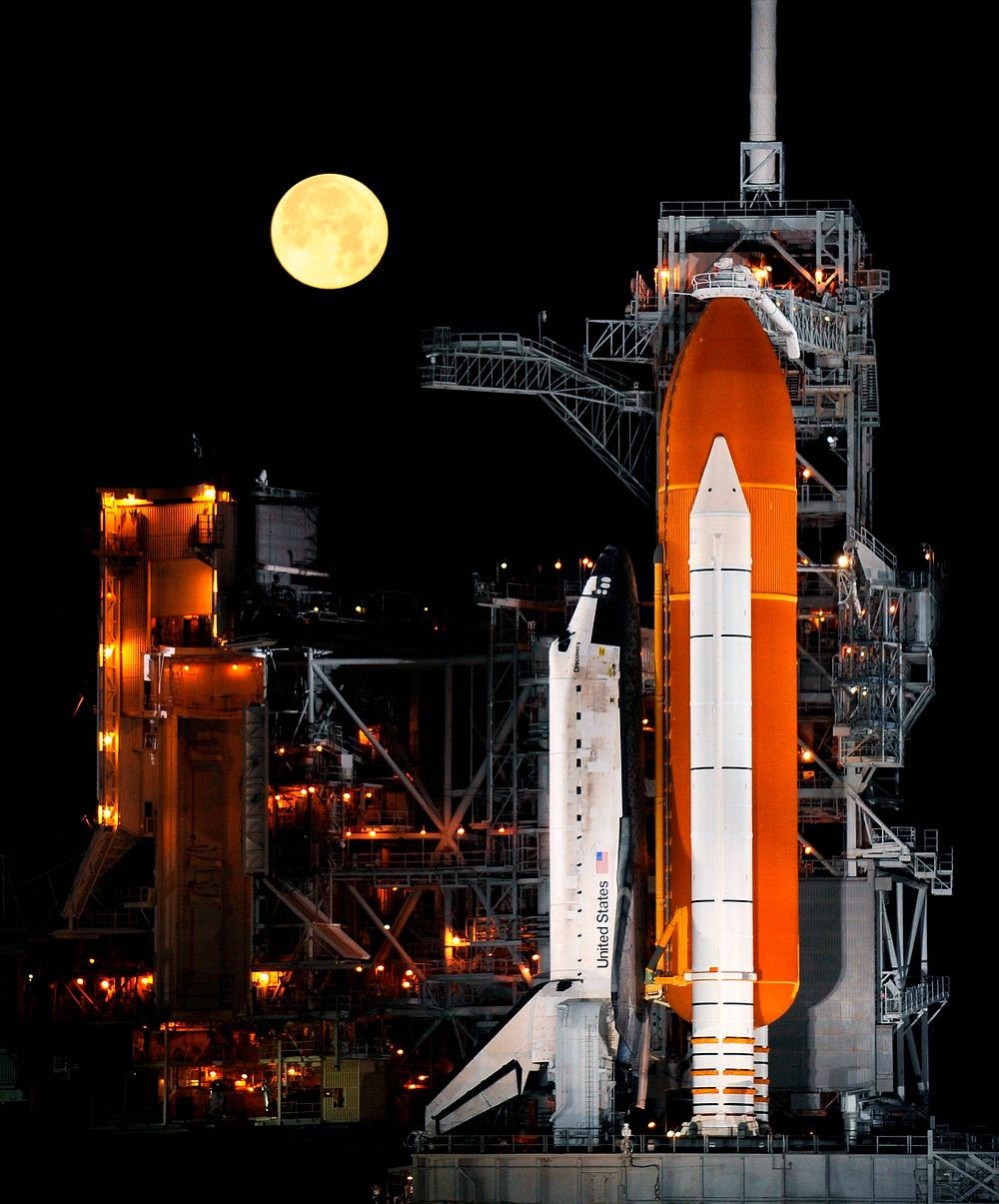 A nearly full Moon sets as the space shuttle Discovery sits atop Launch pad 39A at the Kennedy Space Center in Cape…