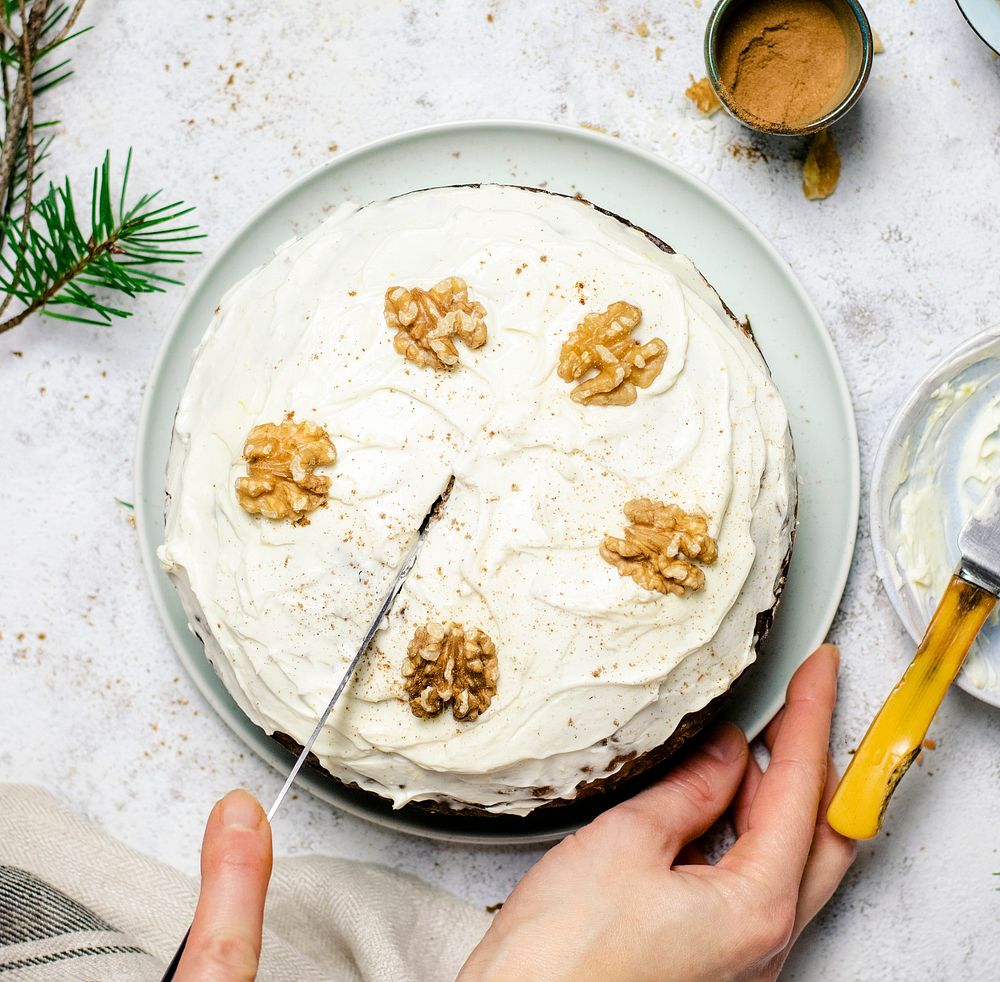 Carrot cake topped with walnuts being sliced