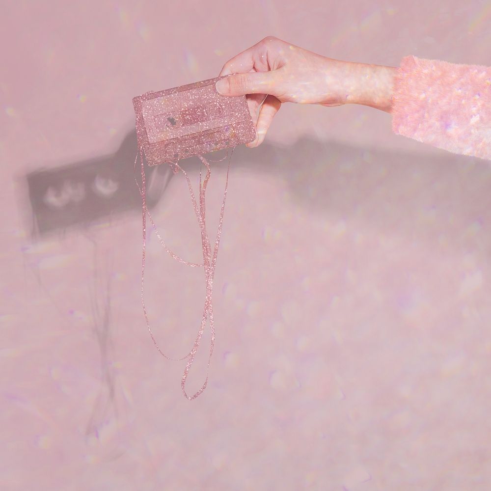 Woman holding a glittery cassette tape against a pink background