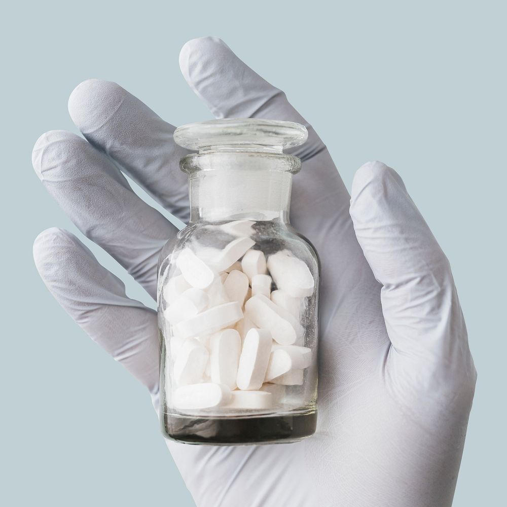 Latex gloves holding a glass jar full of pills 