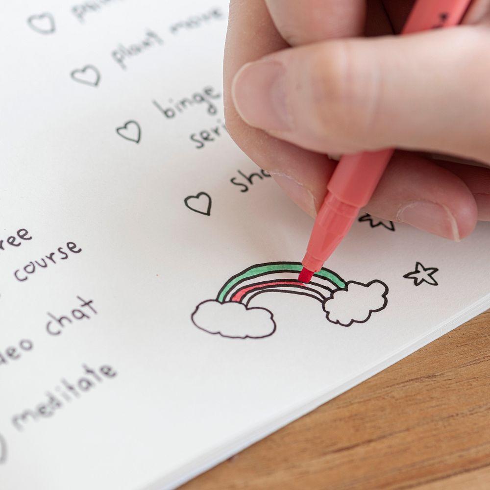 Girl coloring a rainbow doodle in a notebook