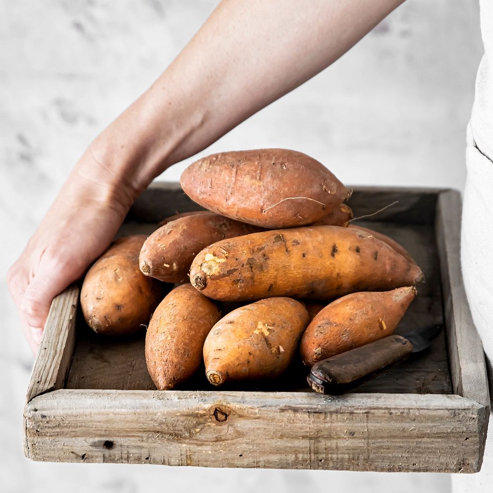 Woman with sweet potatoes in wooden box close up