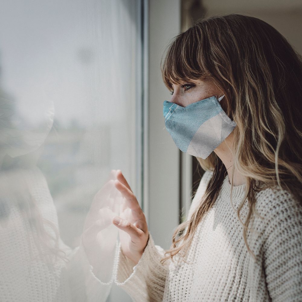 Sick woman wearing face mask staring out the window during a lockdown