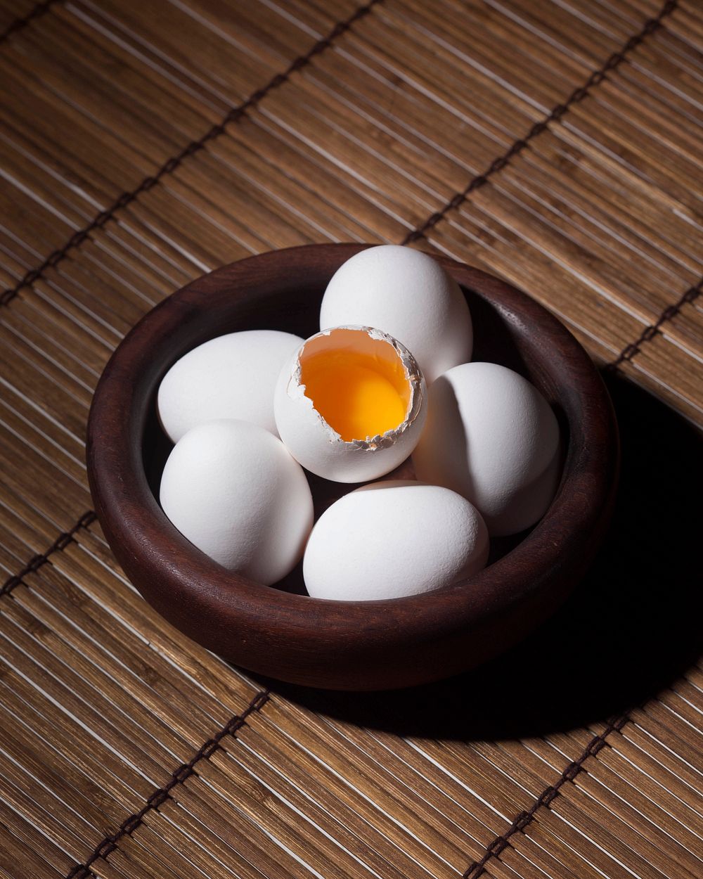 One egg cracks to show the yolk in a bowl full of eggs. Original public domain image from Wikimedia Commons