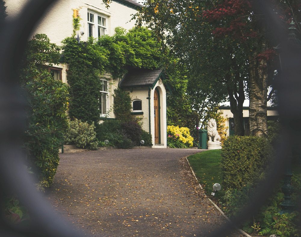 The entrance to a mansion with a beautiful garden seen through the fence. Original public domain image from Wikimedia Commons