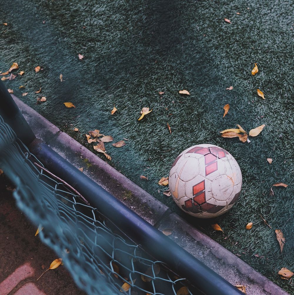 View over the fence on the soccer ball sitting on a green turf pitch. Original public domain image from Wikimedia Commons