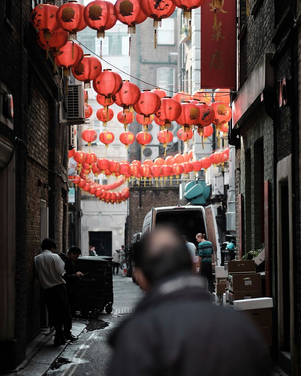 A man looks down an alleyway with strings of paper lanterns hung from the buildings. Original public domain image from…
