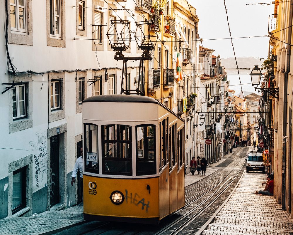 Yellow tram carriage suspended at the top of a narrow street with traditional architecture, Lisbon, Portugal. Original…