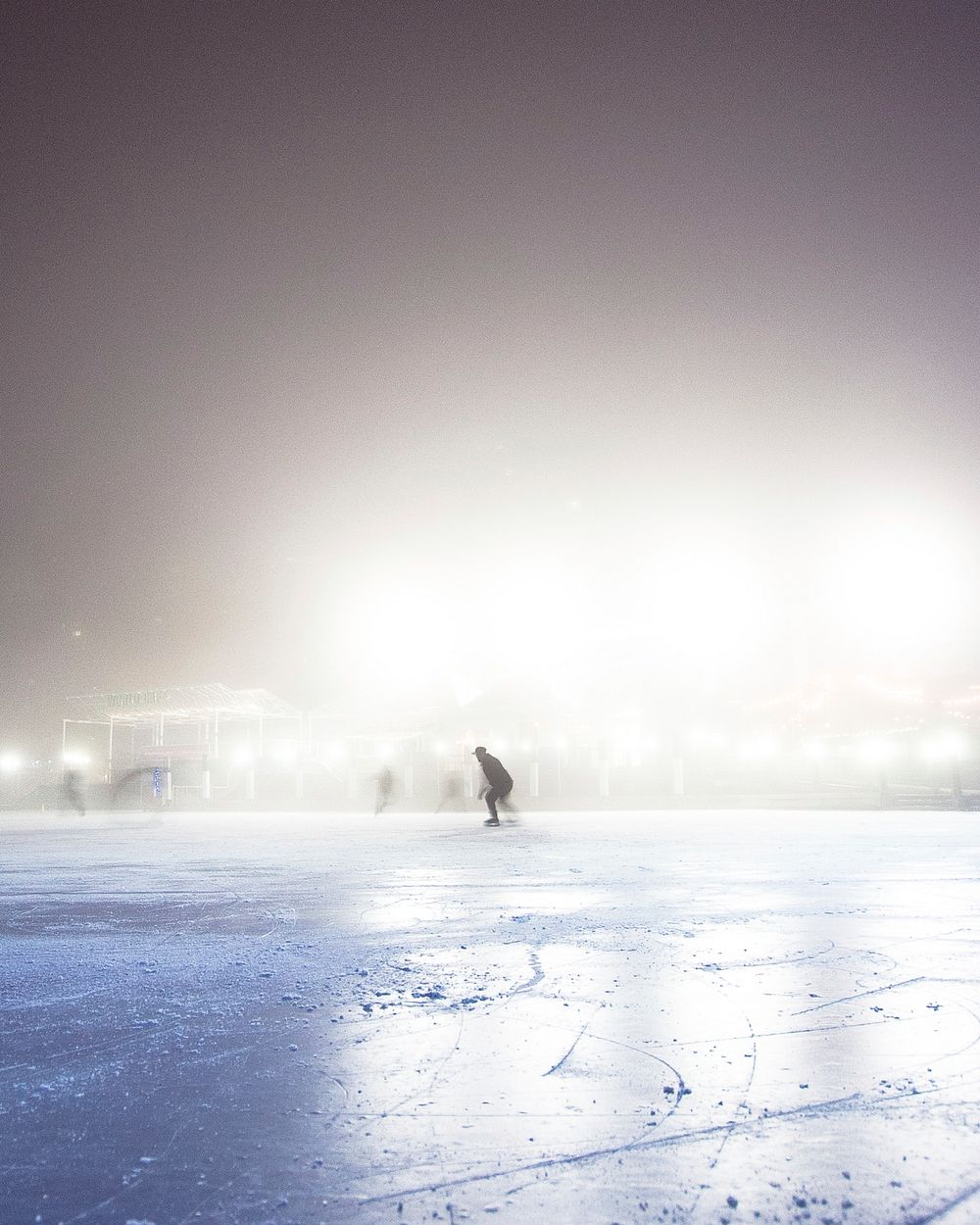 Silhouette of people skating on an ice rink on a misty winter night. Original public domain image from Wikimedia Commons