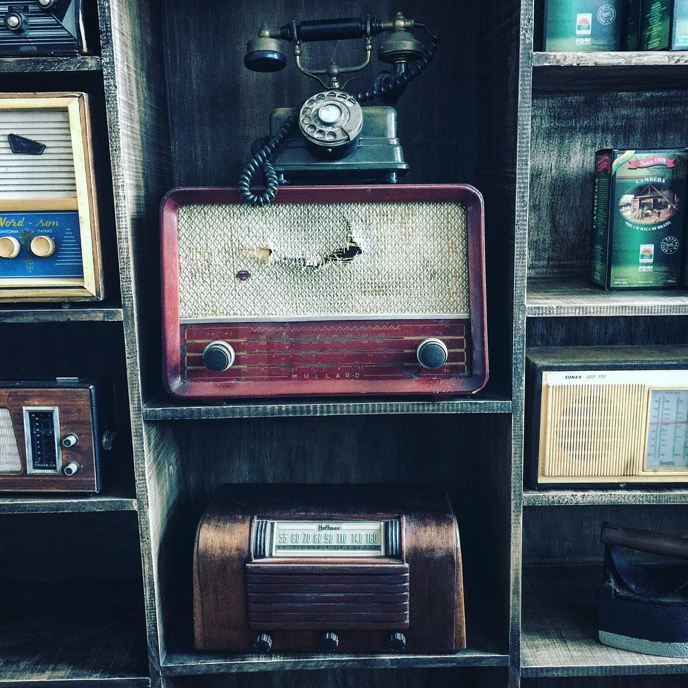 A collection of old radios and an old telephone on shelves. Original public domain image from Wikimedia Commons