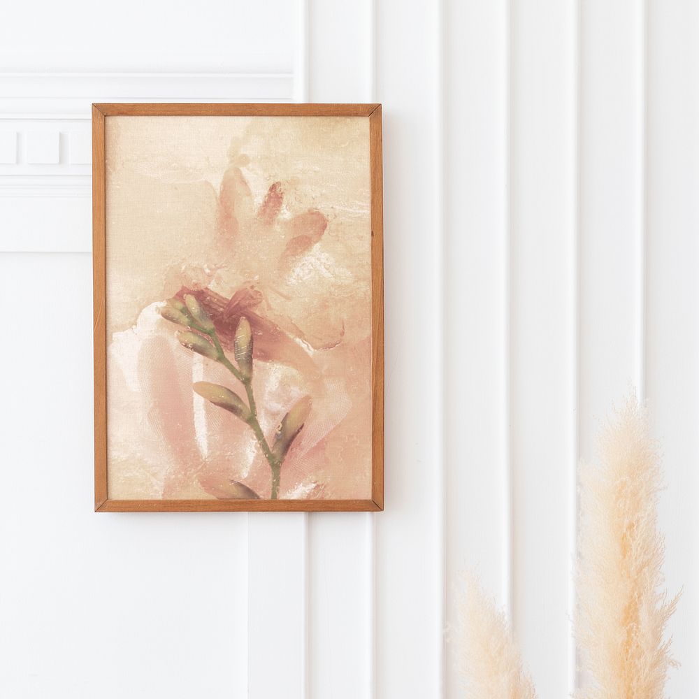 Art in a frame mockup hanging on a white wall by the dried pampas grass 